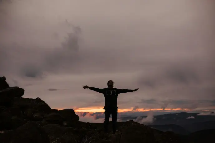 man standing on rock formation under cloudy sky during daytime